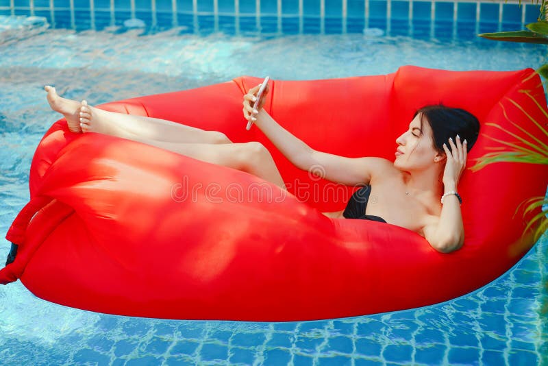 Brunette girl using and talking on her phone while floating in the pool. Brunette girl using and talking on her phone while floating in the pool
