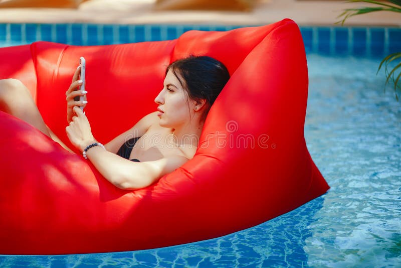 Brunette girl using and talking on her phone while floating in the pool. Brunette girl using and talking on her phone while floating in the pool
