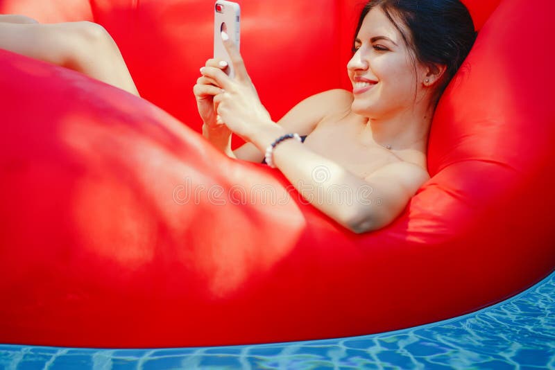 Brunette girl using and talking on her phone while floating in the pool. Brunette girl using and talking on her phone while floating in the pool