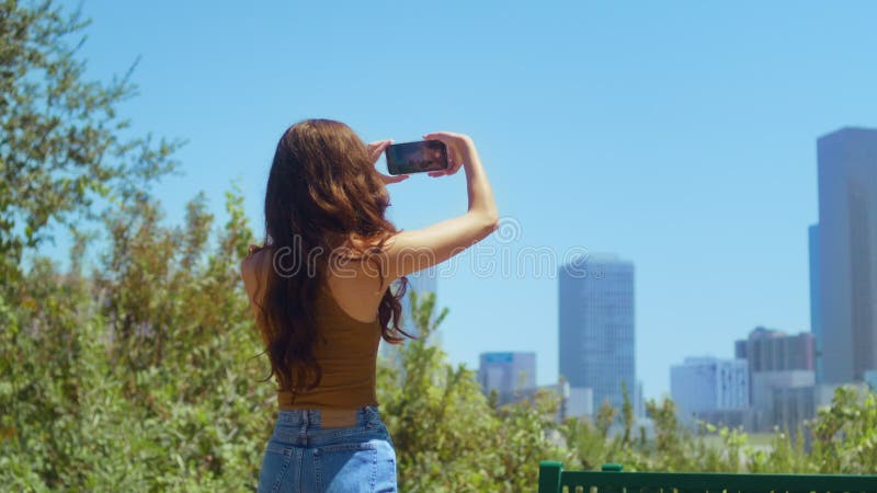 Brunette inconnue prendre en photo paysage urbain debout sur le parc vert arrière vue. banque de vidéos
