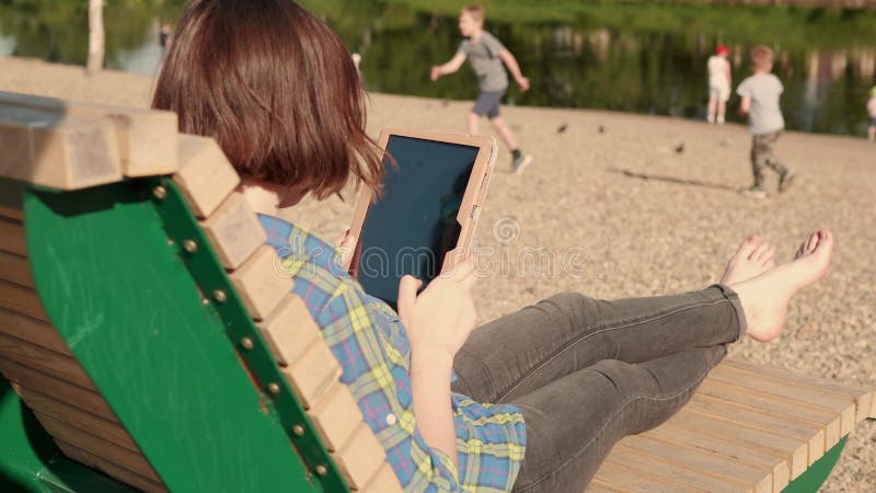 Brunette inconnue utilise une tablette numérique sur la rive du fleuve banque de vidéos