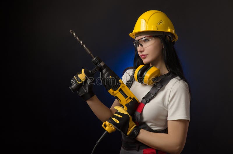 Brunette Mädchen in der speziellen Kleidung und in einer Arbeitskraft in einem Sturzhelm, der auf einem schwarzen Hintergrund mit lizenzfreie stockfotografie