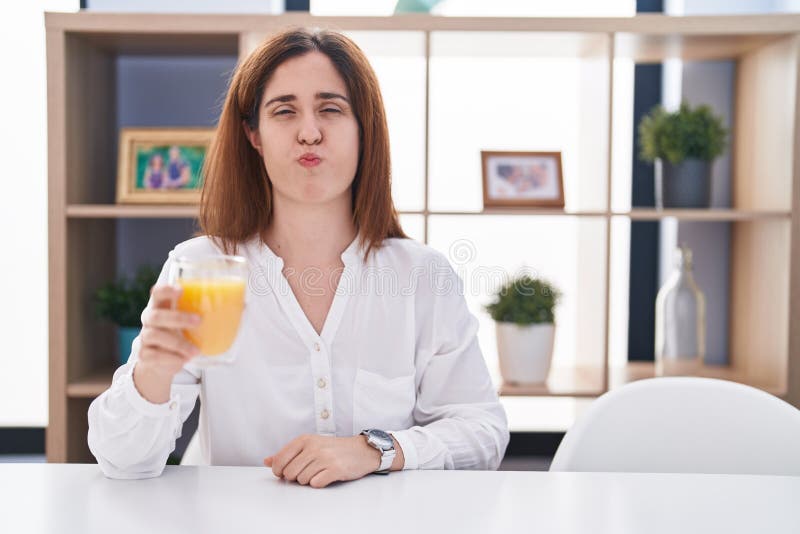 Brunette Woman Drinking Glass of Orange Juice Puffing Cheeks with Funny ...