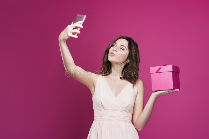 Brunetten i en klänning gör selfie och rymmer en gåvaask arkivfoto Brunetten i en klänning gör selfie och rymmer en gåvaask arkivfoto