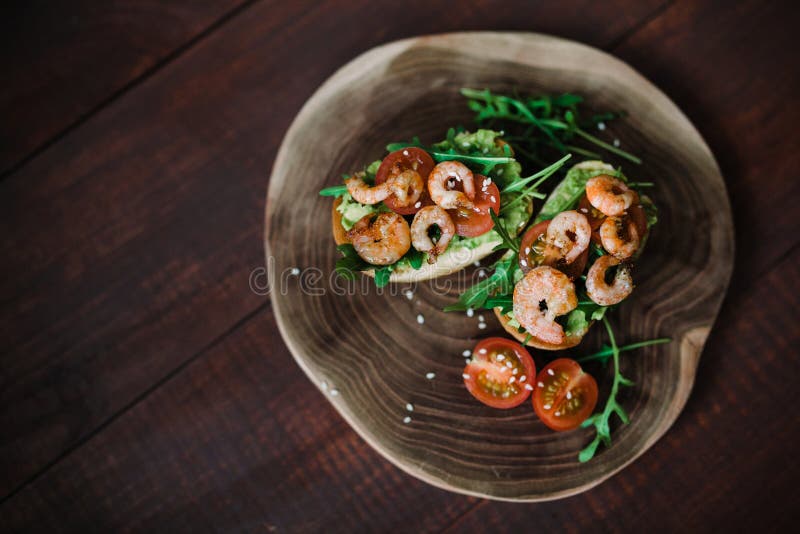 Bruschetta con la gamba y el aguacate en un tablero de madera con el arugula, sésamo, tomates en el fondo de madera para el texto foto de archivo Bruschetta con la gamba y el aguacate en un tablero de madera con el arugula, sésamo, tomates en el fondo de madera para el texto foto de archivo