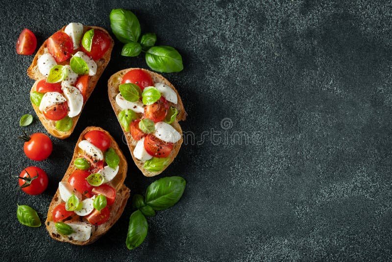 Bruschetta con los tomates, el queso de la mozzarella y la albahaca en un fondo oscuro Aperitivo o bocado italiano tradicional foto de archivo libre de regalías Bruschetta con los tomates, el queso de la mozzarella y la albahaca en un fondo oscuro Aperitivo o bocado italiano tradicional foto de archivo libre de regalías