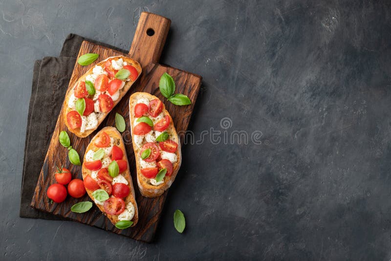 Bruschetta con los tomates, el queso de la mozzarella y la albahaca en una tabla de cortar Aperitivo o bocado italiano tradiciona fotos de archivo libres de regalías Bruschetta con los tomates, el queso de la mozzarella y la albahaca en una tabla de cortar Aperitivo o bocado italiano tradiciona fotos de archivo libres de regalías