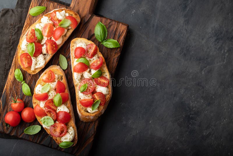 Bruschetta con los tomates, el queso de la mozzarella y la albahaca en una tabla de cortar Aperitivo o bocado italiano tradiciona foto de archivo Bruschetta con los tomates, el queso de la mozzarella y la albahaca en una tabla de cortar Aperitivo o bocado italiano tradiciona foto de archivo