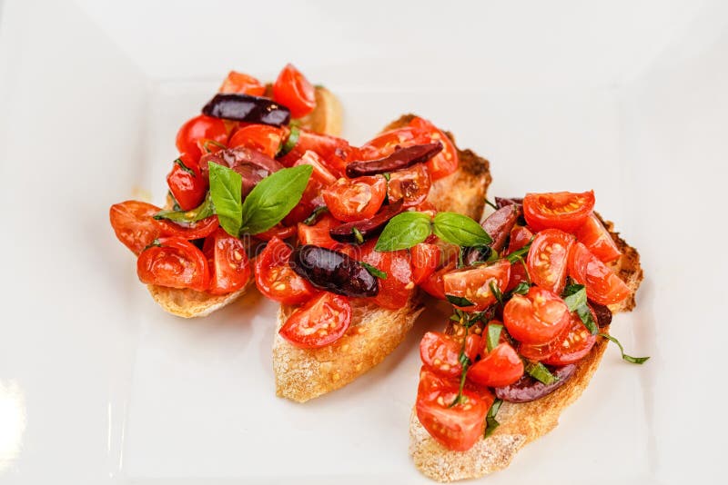 Bruschetta italiana con i pomodori, il basilico e l'oliva tagliati immagine stock Bruschetta italiana con i pomodori, il basilico e l'oliva tagliati immagine stock