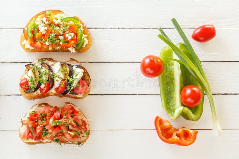 Bruschetta med ny tomater och ost, aubergine och mozzarella, söt peppar och getost på vita bräden royaltyfri fotografi Bruschetta med ny tomater och ost, aubergine och mozzarella, söt peppar och getost på vita bräden royaltyfri fotografi