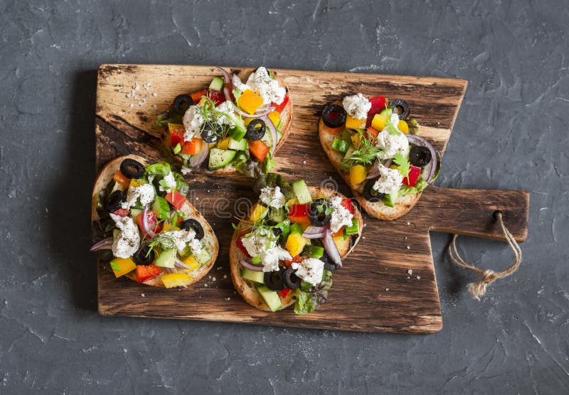 Bruschette grecque de style de salade sur une planche à découper en bois, sur le fond foncé, vue supérieure photos stock Bruschette grecque de style de salade sur une planche à découper en bois, sur le fond foncé, vue supérieure photos stock