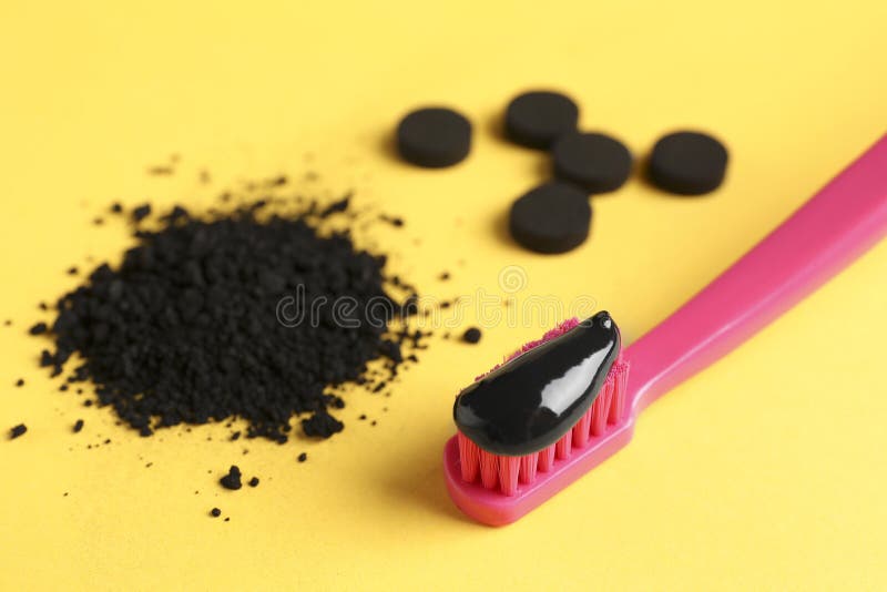 Brush with Charcoal Toothpaste, Powder and Tablets on Yellow Background