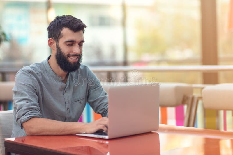 Brustbild des erfolgreichen bärtigen Designers, der an der Kamera beim Arbeiten an freiberuflich tätigem am netbook lächelt lizenzfreies stockfoto Brustbild des erfolgreichen bärtigen Designers, der an der Kamera beim Arbeiten an freiberuflich tätigem am netbook lächelt lizenzfreies stockfoto