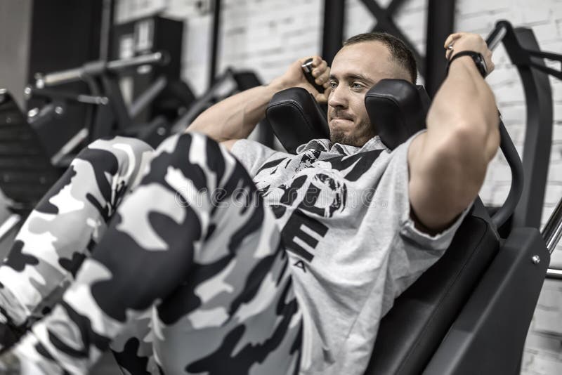 Tenso hombre tiene pierna para presionar ejercicio sobre el entrenador en gimnasia.