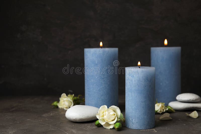Brännande stearinljus, brunnsortstenar och blommor på mörka grå färger, utrymme för text arkivbilder Brännande stearinljus, brunnsortstenar och blommor på mörka grå färger, utrymme för text arkivbilder