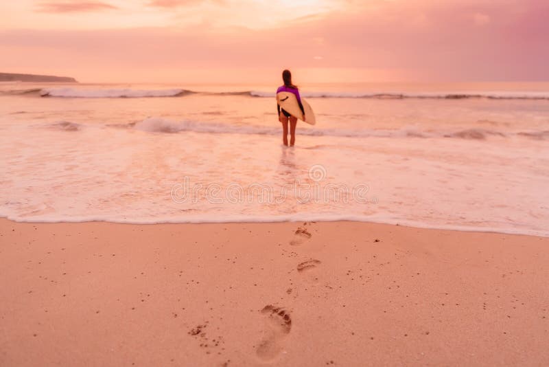 Bränningflickan med surfingbrädan går till att surfa Surfarekvinna på en strand på solnedgången eller soluppgång