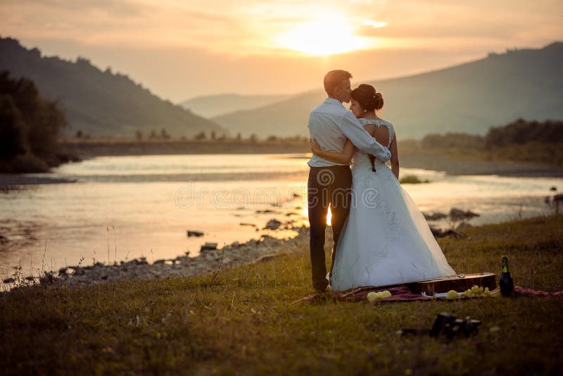 Bräutigam küsst weich seine herrliche Braut in der Stirn während des Sonnenuntergangs Hochzeitspicknick auf der Flussbank stockfotos Bräutigam küsst weich seine herrliche Braut in der Stirn während des Sonnenuntergangs Hochzeitspicknick auf der Flussbank stockfotos