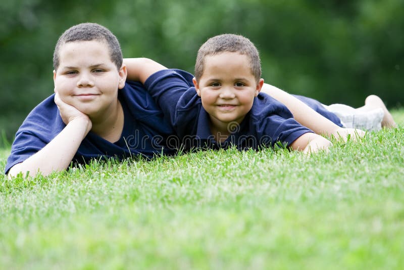 Two brothers lying on their fronts on fresh green grass. Two brothers lying on their fronts on fresh green grass