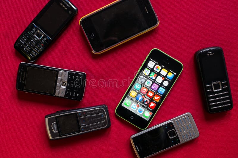 BUCAREST, ROMANIA - 17 MARZO 2014: La foto del iphone contro vecchio Nokia telefona su un fondo rosso che mostra l'evoluzione del immagine stock libera da diritti BUCAREST, ROMANIA - 17 MARZO 2014: La foto del iphone contro vecchio Nokia telefona su un fondo rosso che mostra l'evoluzione del immagine stock libera da diritti