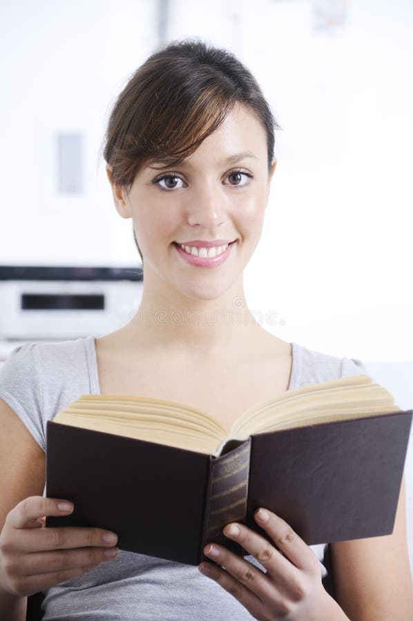 Woman reading book in home interior, smiling and looking in camera; concept of relax and entertainment. Woman reading book in home interior, smiling and looking in camera; concept of relax and entertainment