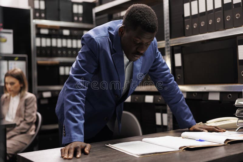 Bookkeeper working at bureaucracy report, analyzing administrative files late at night in storage room. African american businessman searching for bookkeeping record in corporate depository. Bookkeeper working at bureaucracy report, analyzing administrative files late at night in storage room. African american businessman searching for bookkeeping record in corporate depository