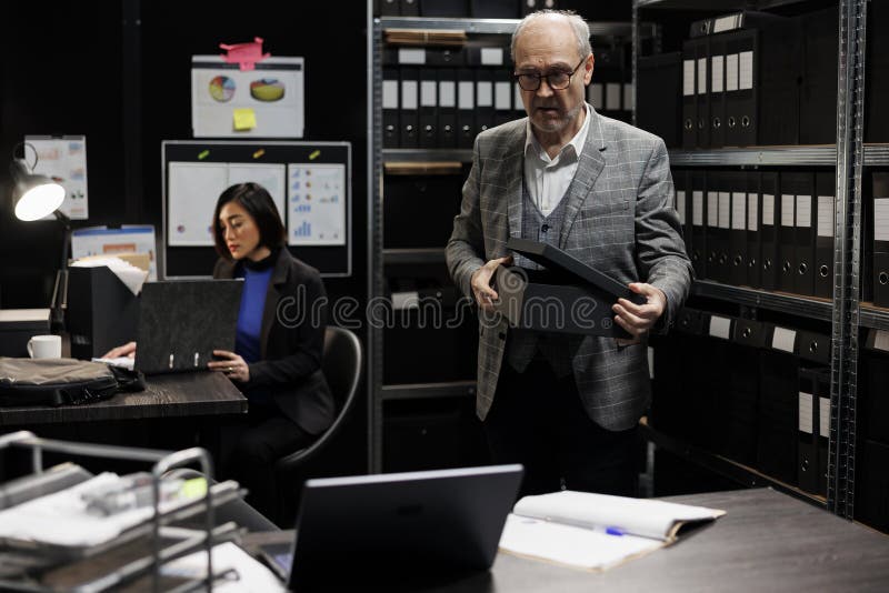 Senior manager bookkeeper storing annual profit revenue files before official business inspection. Bureaucratic workplace filled with flowcharts and document folders on depository cabinet shelves. Senior manager bookkeeper storing annual profit revenue files before official business inspection. Bureaucratic workplace filled with flowcharts and document folders on depository cabinet shelves