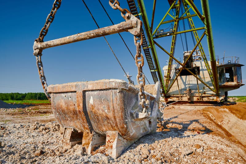 Bucket of old walking excavator digging calx in quarry against bright blue sky. Heavy machinery mines minerals in countryside closeup