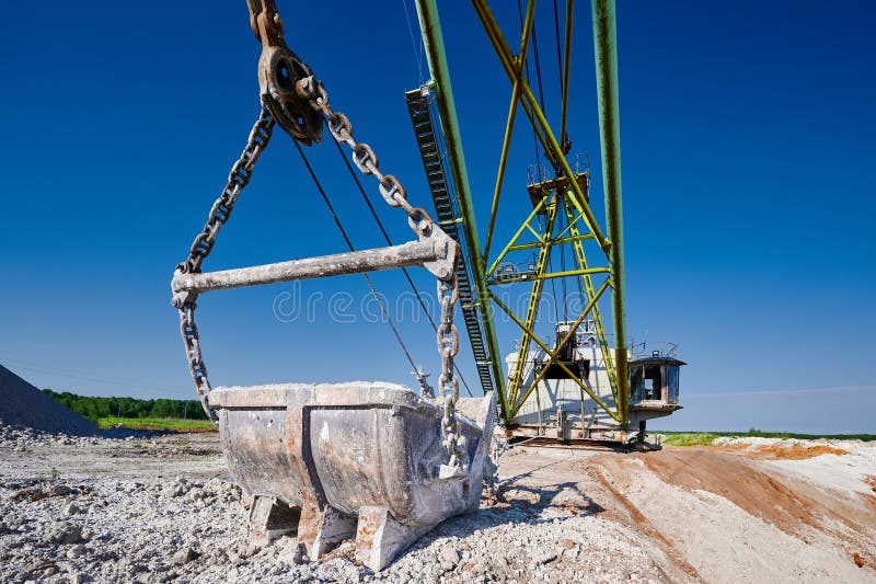 Bucket of old walking excavator digging calx in quarry against bright blue sky. Heavy machinery mines minerals in countryside closeup