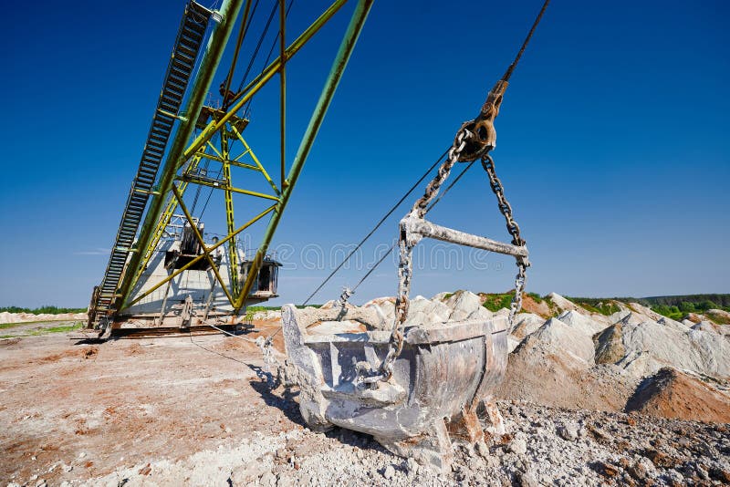 Bucket of old walking excavator digging calx in quarry against bright blue sky. Heavy machinery mines minerals in countryside closeup