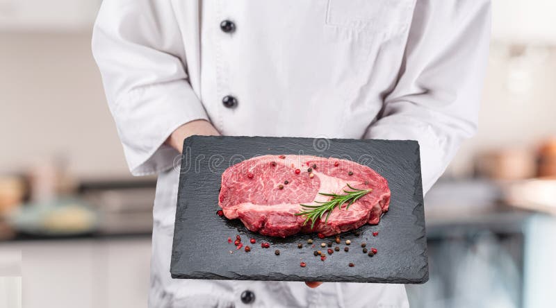 Bucătarul ține friptura crudă de friptură cu condimente și ierburi pe tablă neagră pentru servit royalty free stock photography
