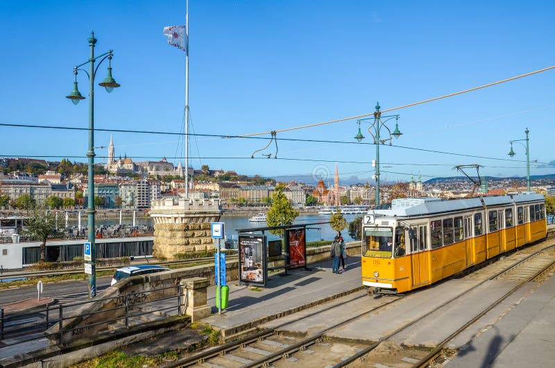 Budapest, Ungheria - 6 nov 2019: Tram giallo alla stazione pubblica Danubio e centro storico con la Bastione di Fisherman immagine stock Budapest, Ungheria - 6 nov 2019: Tram giallo alla stazione pubblica Danubio e centro storico con la Bastione di Fisherman immagine stock