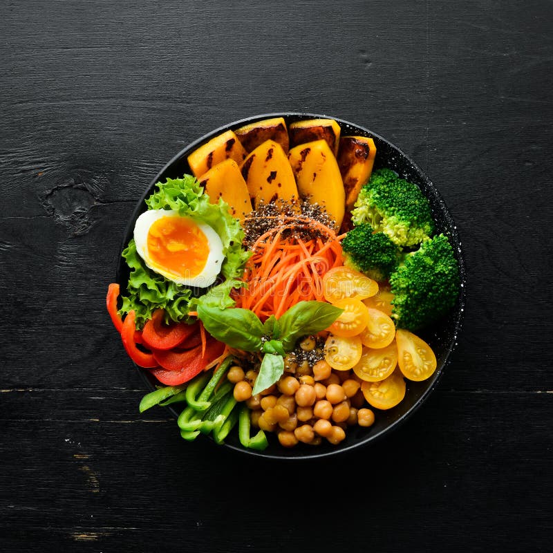 Buddha bowl: pumpkin, broccoli, egg, tomatoes, carrots, paprika in a black plate on a black background.