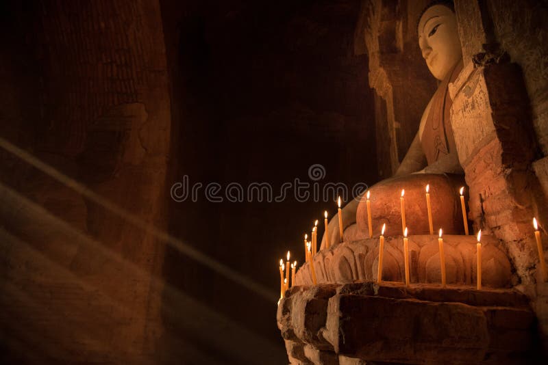 Buddha statue inside the pagoda with candle light under the ray of light