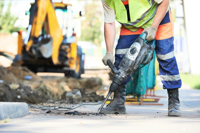 Builder worker with pneumatic hammer drill equipment breaking asphalt at road construction site. Builder worker with pneumatic hammer drill equipment breaking asphalt at road construction site