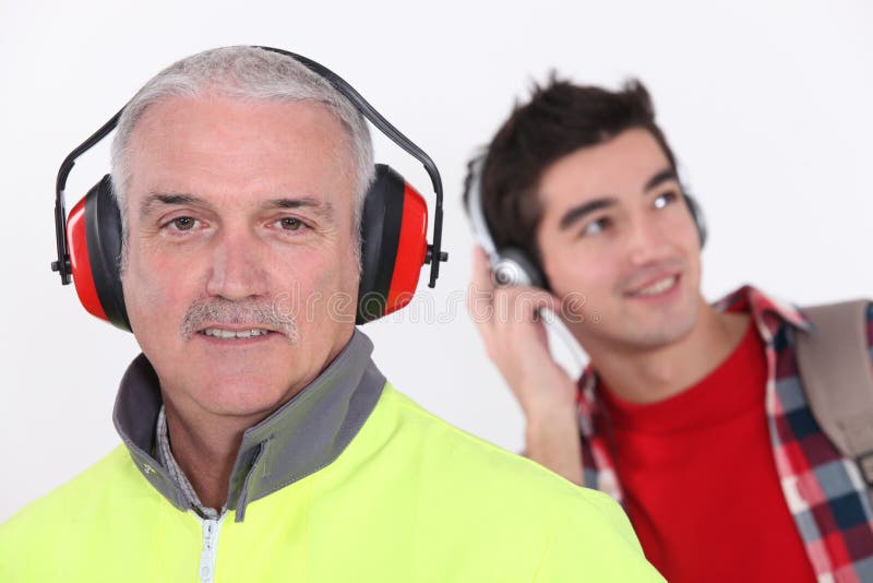 Builder wearing ear protection stood in front of teenage boy. Builder wearing ear protection stood in front of teenage boy