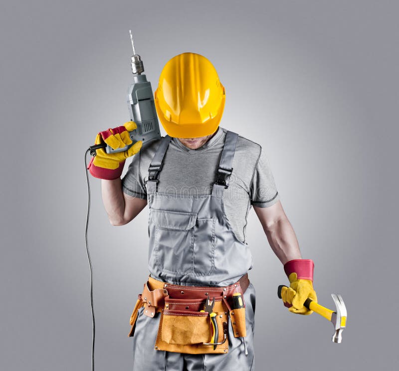 builder in a helmet with a hammer and a drill on grey isolated background. builder in a helmet with a hammer and a drill on grey isolated background