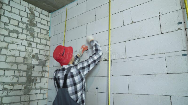 Budowniczy w pracy odzieży i czerwonej nakrętce wkłada budowa kahaty w blok ścianę