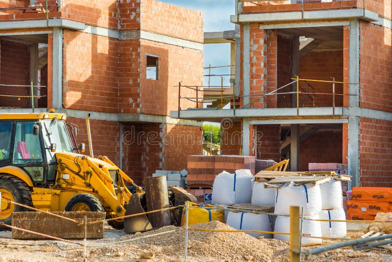 Budowy czerwonej cegły mieszkaniowi domy miejscy, betonowi filary, czerparka, stosy materiały, niedokończona nowa budowa obraz stock Budowy czerwonej cegły mieszkaniowi domy miejscy, betonowi filary, czerparka, stosy materiały, niedokończona nowa budowa obraz stock