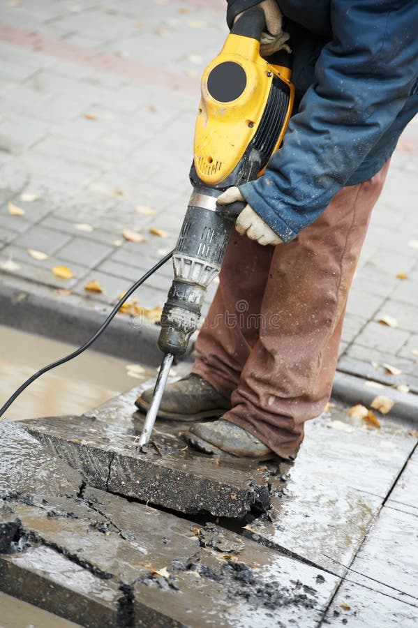 Builder worker with pneumatic hammer drill equipment breaking asphalt at construction site. Builder worker with pneumatic hammer drill equipment breaking asphalt at construction site