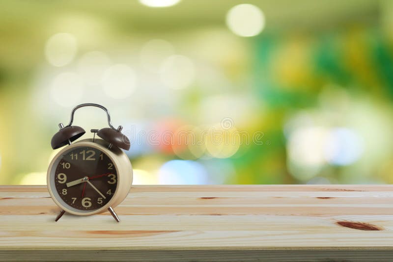 Budzik na drewnianym podłogi i zieleni bokeh tle z kopii przestrzenią, ranek budzi się jest jaskrawym powietrzem natura zdjęcia stock Budzik na drewnianym podłogi i zieleni bokeh tle z kopii przestrzenią, ranek budzi się jest jaskrawym powietrzem natura zdjęcia stock