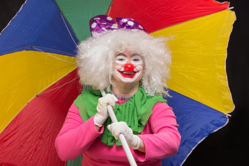 Buen payaso divertido alegre con un paraguas multicolor en un negro fotografía de archivo Buen payaso divertido alegre con un paraguas multicolor en un negro fotografía de archivo