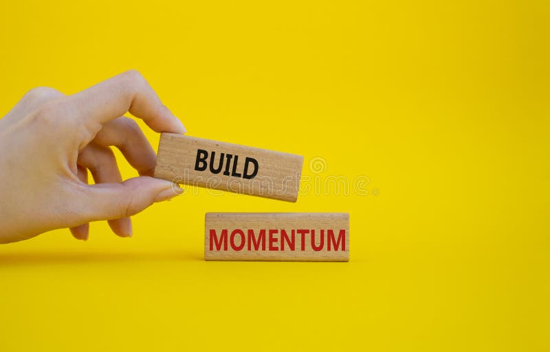 Build momentum symbol. Wooden blocks with words Build momentum. Beautiful yellow background. Businessman hand. Business and Build stock photo