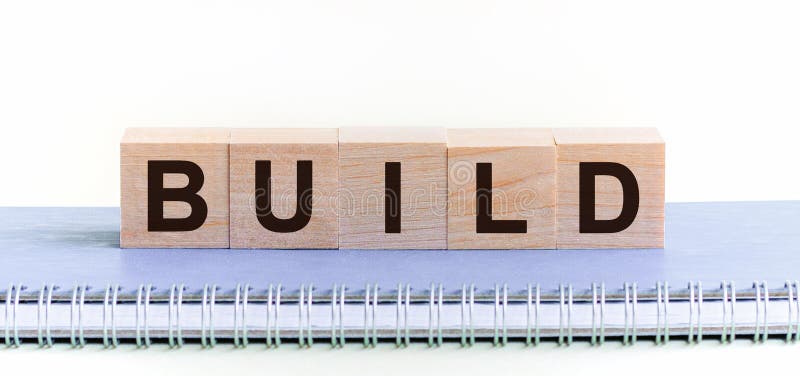 BUILD - a word made of wooden blocks with black letters, a row of blocks is located on a blue Notepad. White background, front view