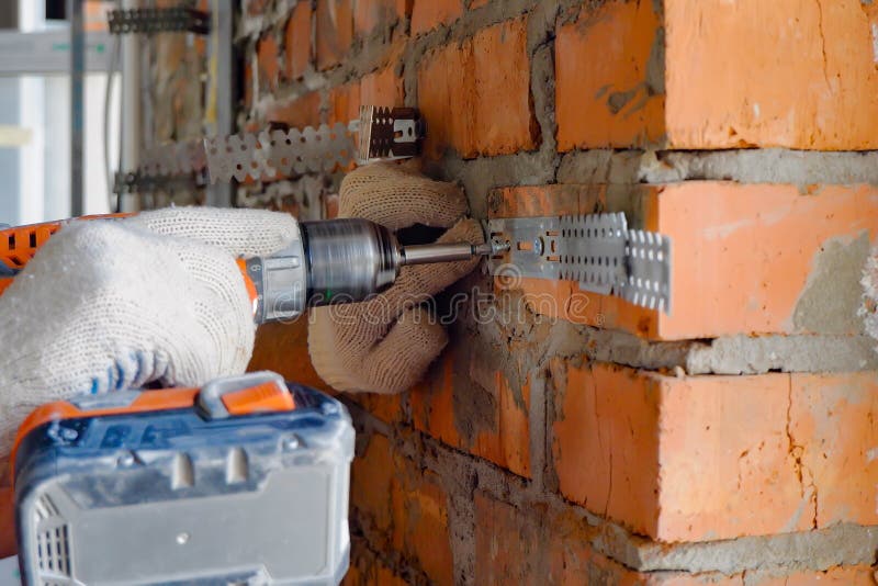 A Builder Attaches a Construction Suspension for Drywall To a Brick