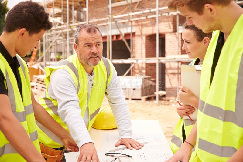 Builder On Building Site Discussing Work With Apprentice