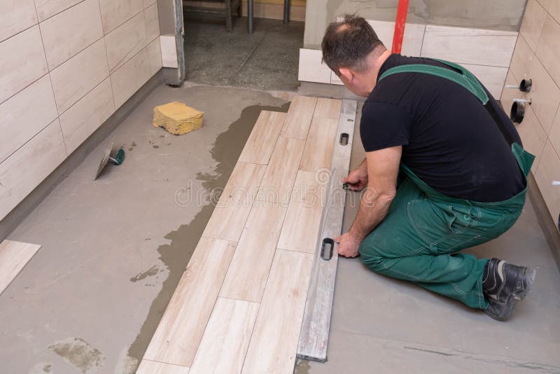 A Builder Checks the Surface Level of Tiles Laid on the Bathroom Floor