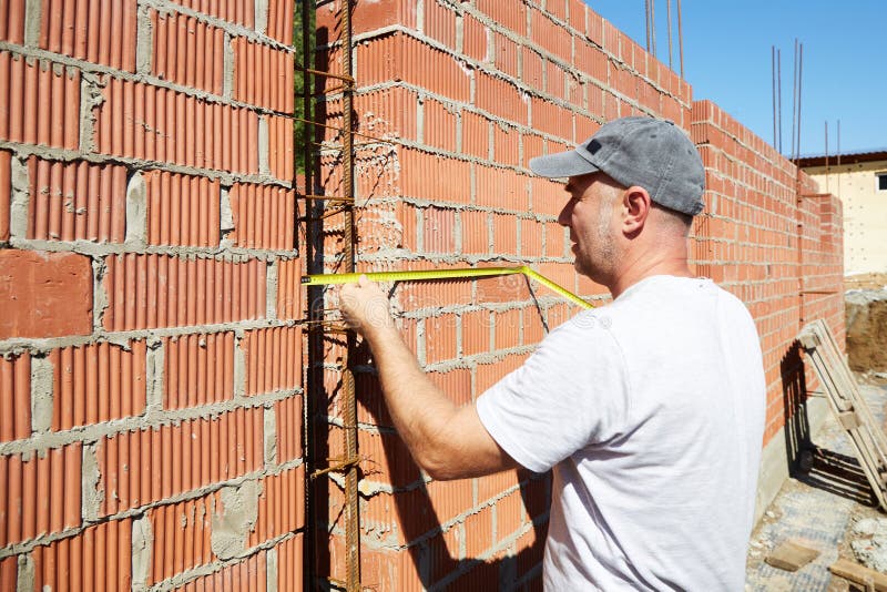 A construction worker is measuring a brick wall at a building site stock photography