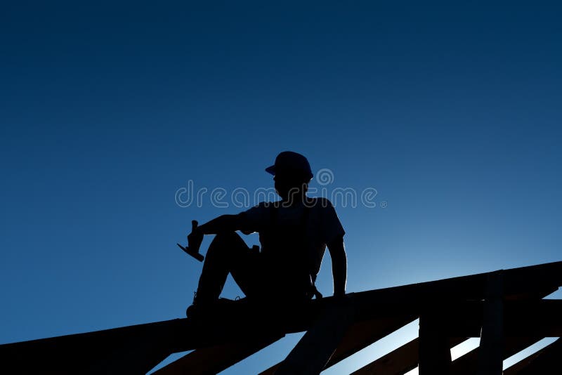 Builder or carpenter resting on top of roof structure - silhouette with strong back light. Builder or carpenter resting on top of roof structure - silhouette with strong back light