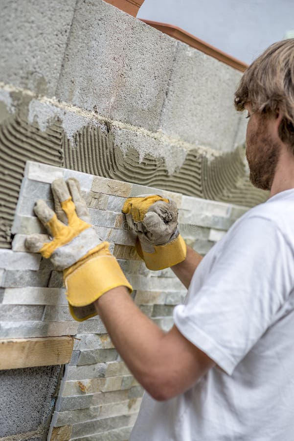 Builder tiling a wall with ornamental tiles pushing the tile into the cement on the wall with his gloved fist in a DIY, renovation or construction concept. Bricklayer tiler stock images, royalty-free photos and pictures