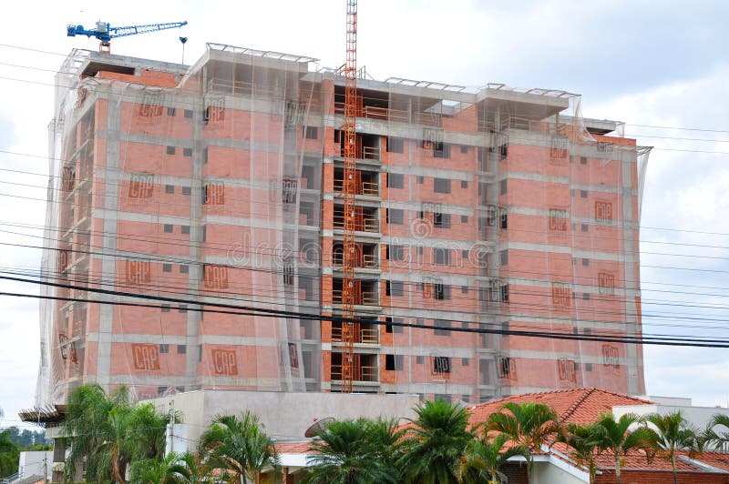 Building facade under construction, panoramic view with protective screen and overhead crane, in area of houses, urban neighborhoo